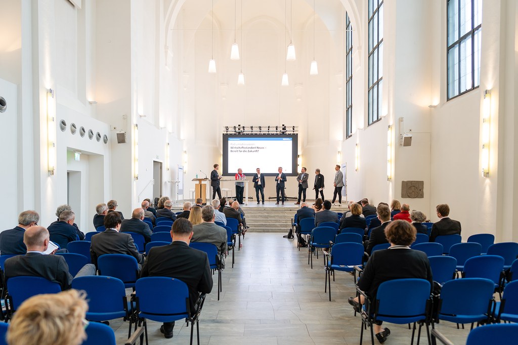 neusser-zukunftskongress-2022_06b.jpg Die Panelteilnehmer stehen auf der Bühne des Zeughauses und diskutieren.